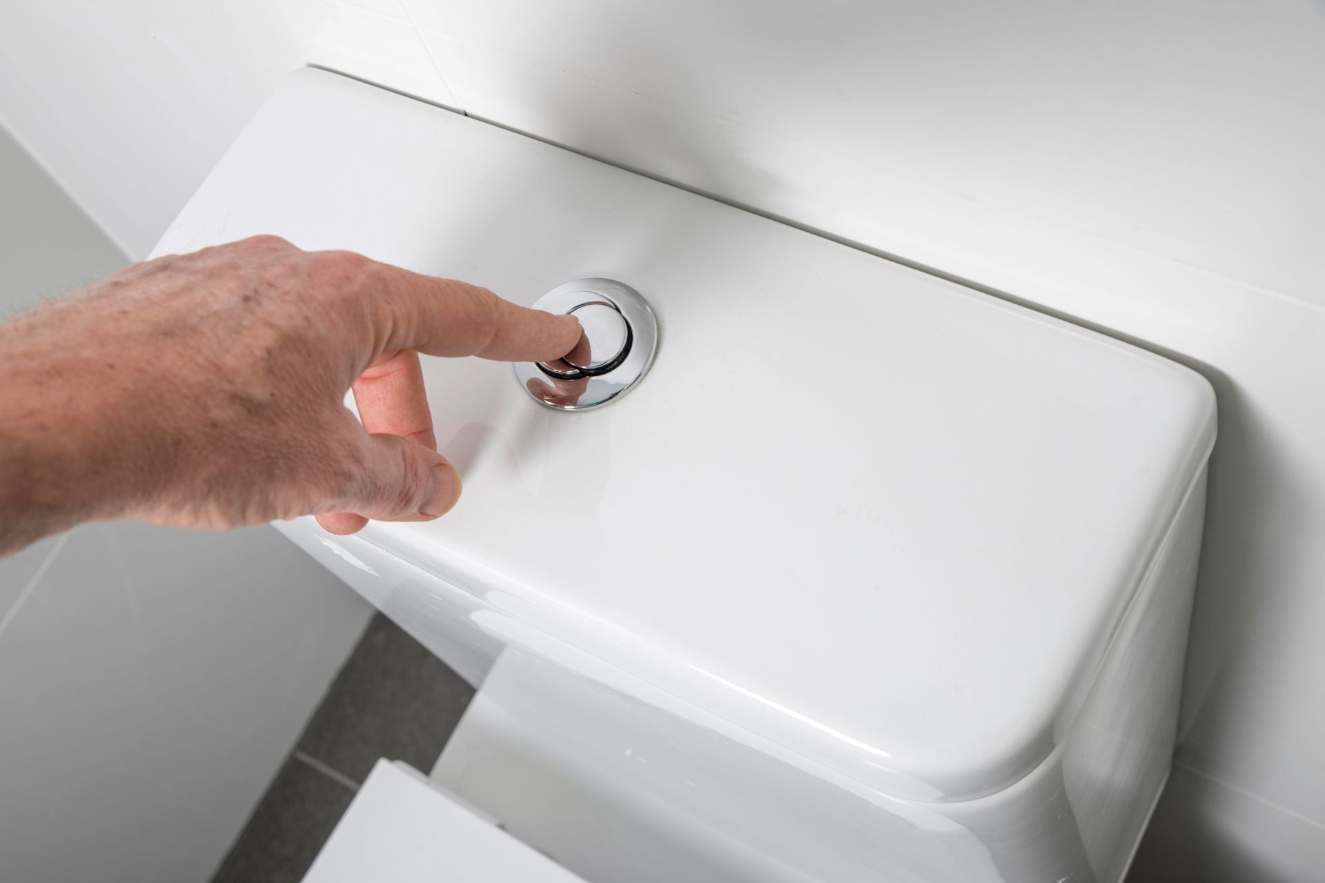 A person pressing down on a toilet tank’s dual flush button