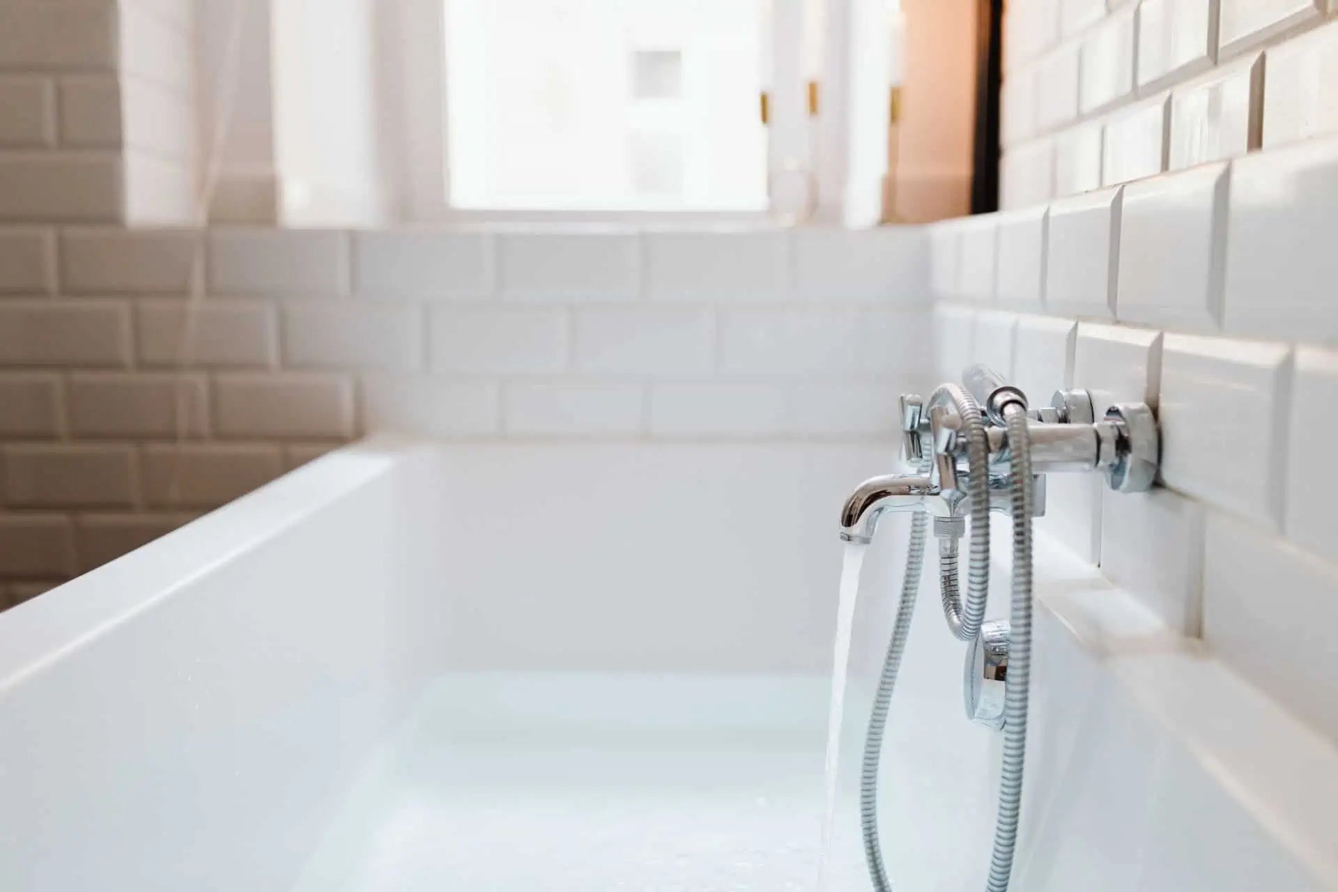 A stainless steel double-handle bathtub faucet fills a tub with water