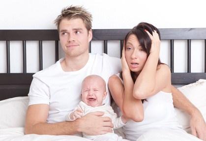 verzweifelte Eltern mit schreiendem Baby sitzen im Familienbett