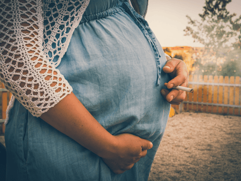 schwangere Frau hält Zigarette in der Hand