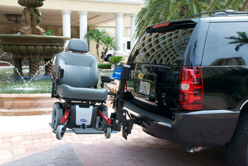 a power wheelchair is stowed on an exterior hitch lift on the back of a black SUV