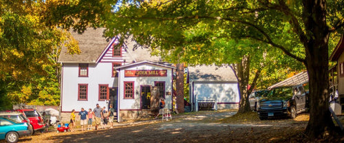 customers gather around the entrance to BF Clyde cider mill, a white building with red trim surrounded by trees just beginning to change color
