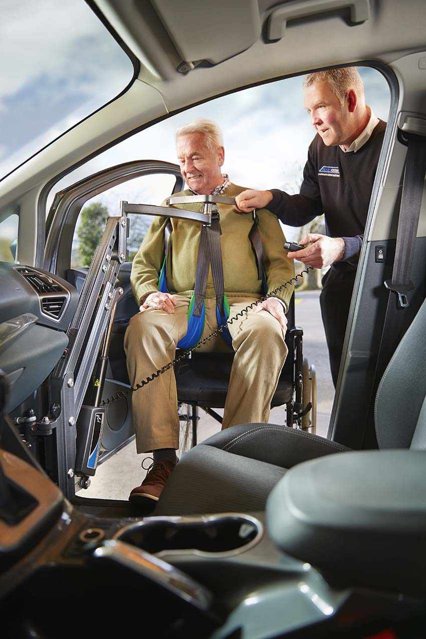 an elderly man being assisted to transfer into a car from a manual wheelchair using a Smart Transfer hoist