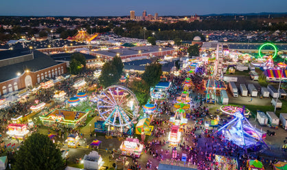 The Big E fairgrounds are viewed from above at night, swarming with people and lit with colorful neon lights