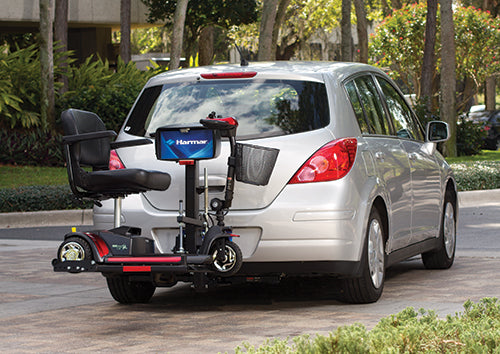 a red mobility scooter is docked on an exterior vehicle lift at the rear of a silver station wagon