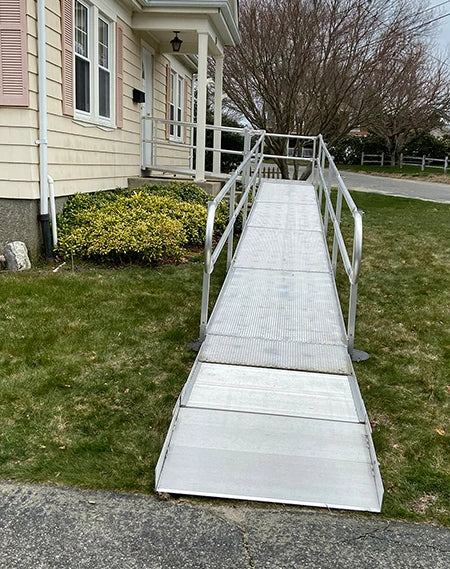 a silver modular aluminum ramp is installed in front of a cream house and runs from the front door towards the viewer