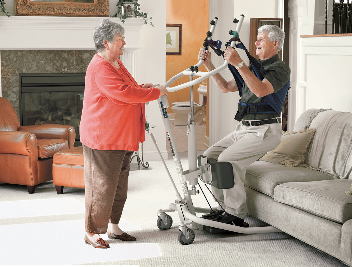 elderly woman helping elderly man stand up from a couch using a sit-to-stand patient lift