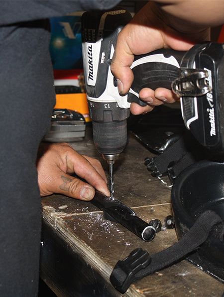 closeup view of someone using a power drill to drill a hole in a piece of black metal pipe