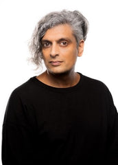 A colour photo of poet Kazim Ali smiling subtly, posing in a black sweater.