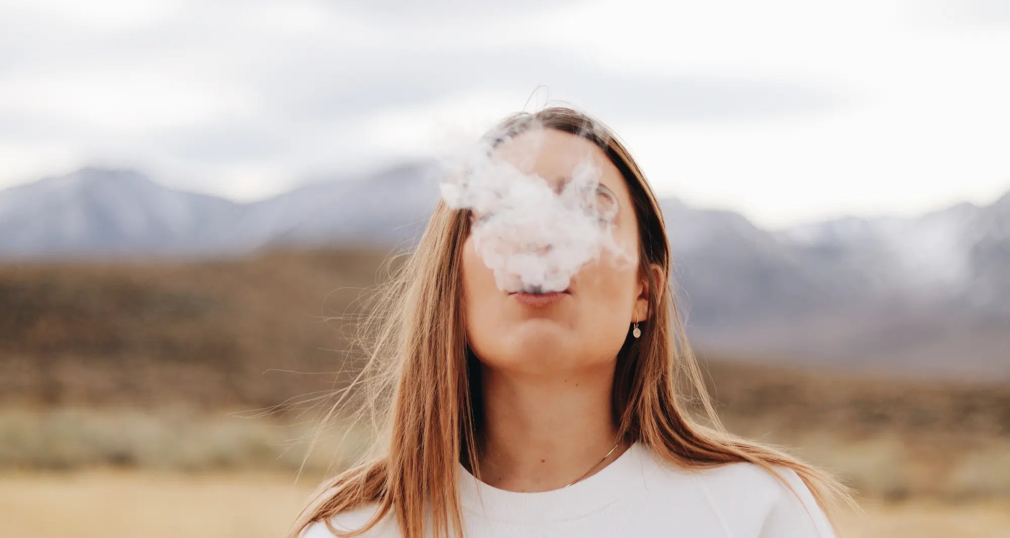 a woman smokes a cigarette in the air while standing in a field