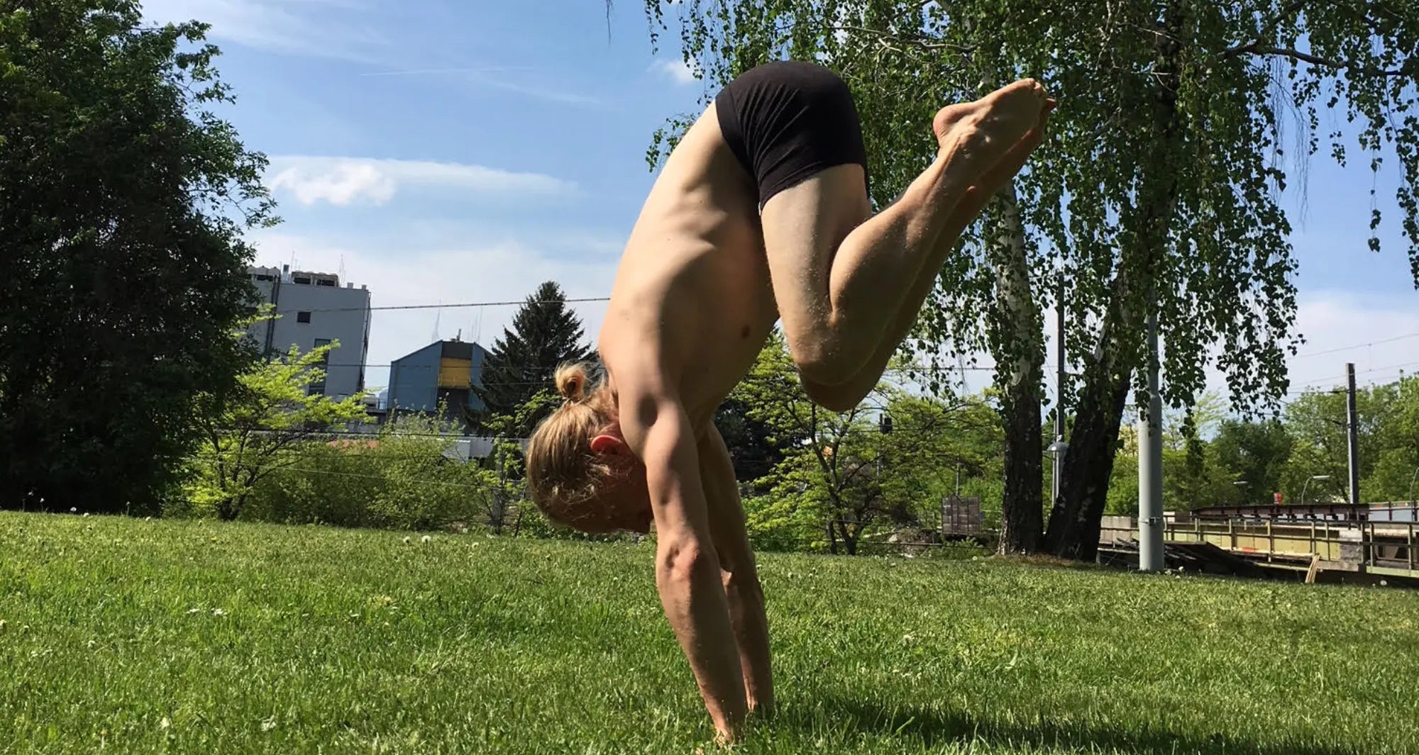 A man outside attempting to do a hand stand, wearing  black hemp boxer briefs