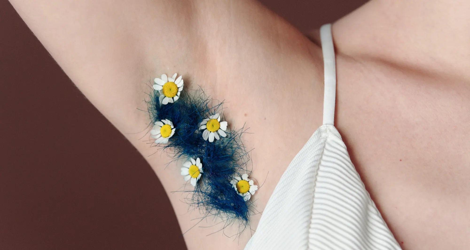 a close up of the armpit of a white woman with dark blue dyed armpit hair and tiny yellow and white flowers placed in it