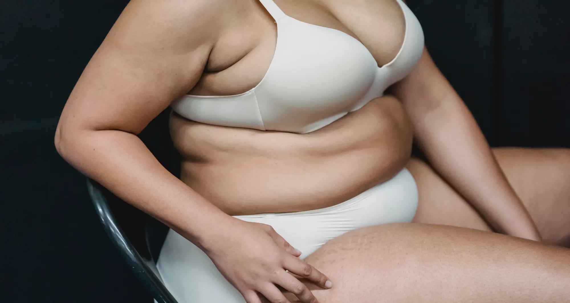 A woman sitting on a black chair  wearing white bra and a white underwear