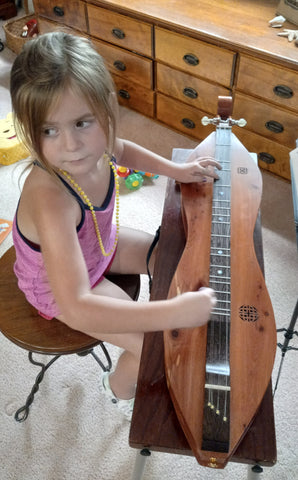 five year old girl playing a dulimer her grandpa made for her