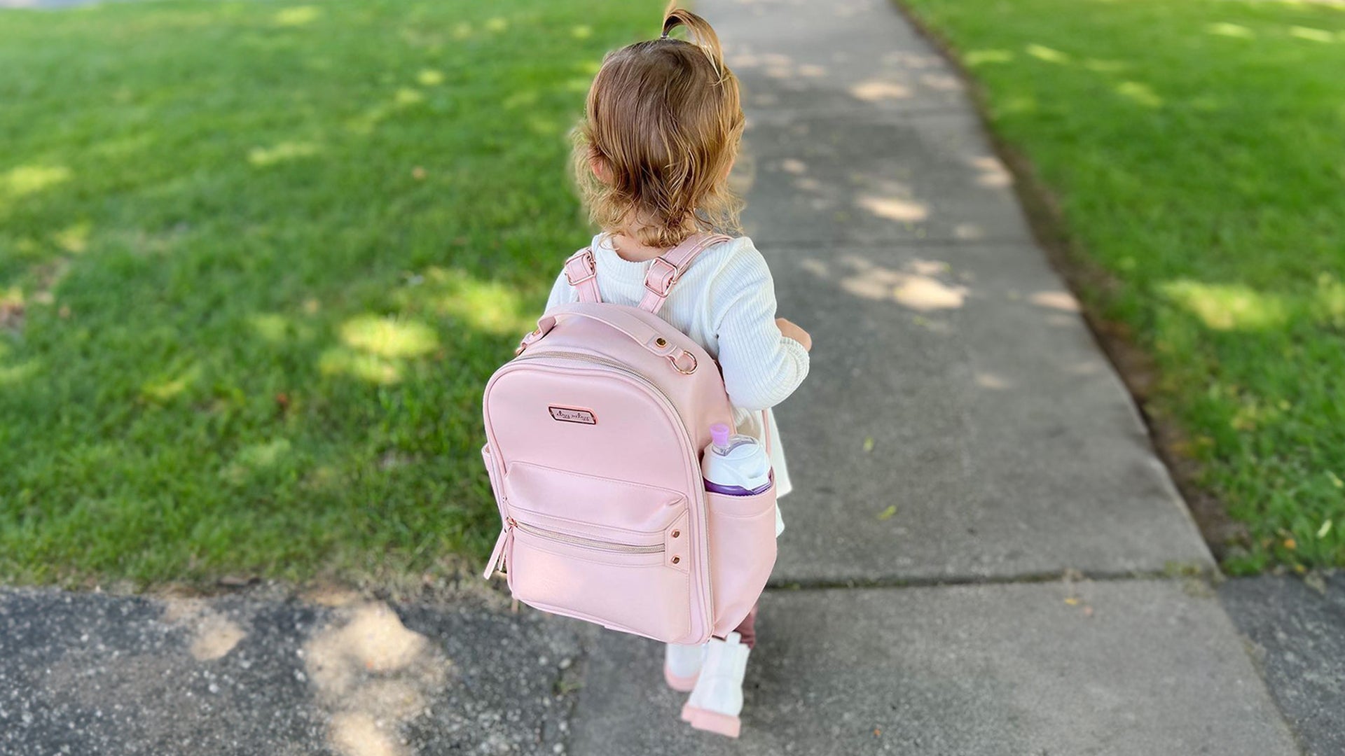 Itzy Ritzy Mini Diaper Bag in Blush color worn by a toddler on her back