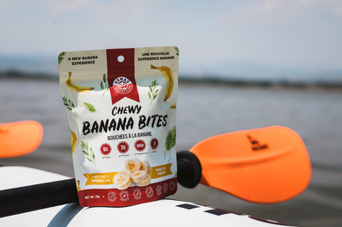 Nomad Nutrition Chewy Banana Bites packaging on a boat out in the open waters with paddles visible in the background. 