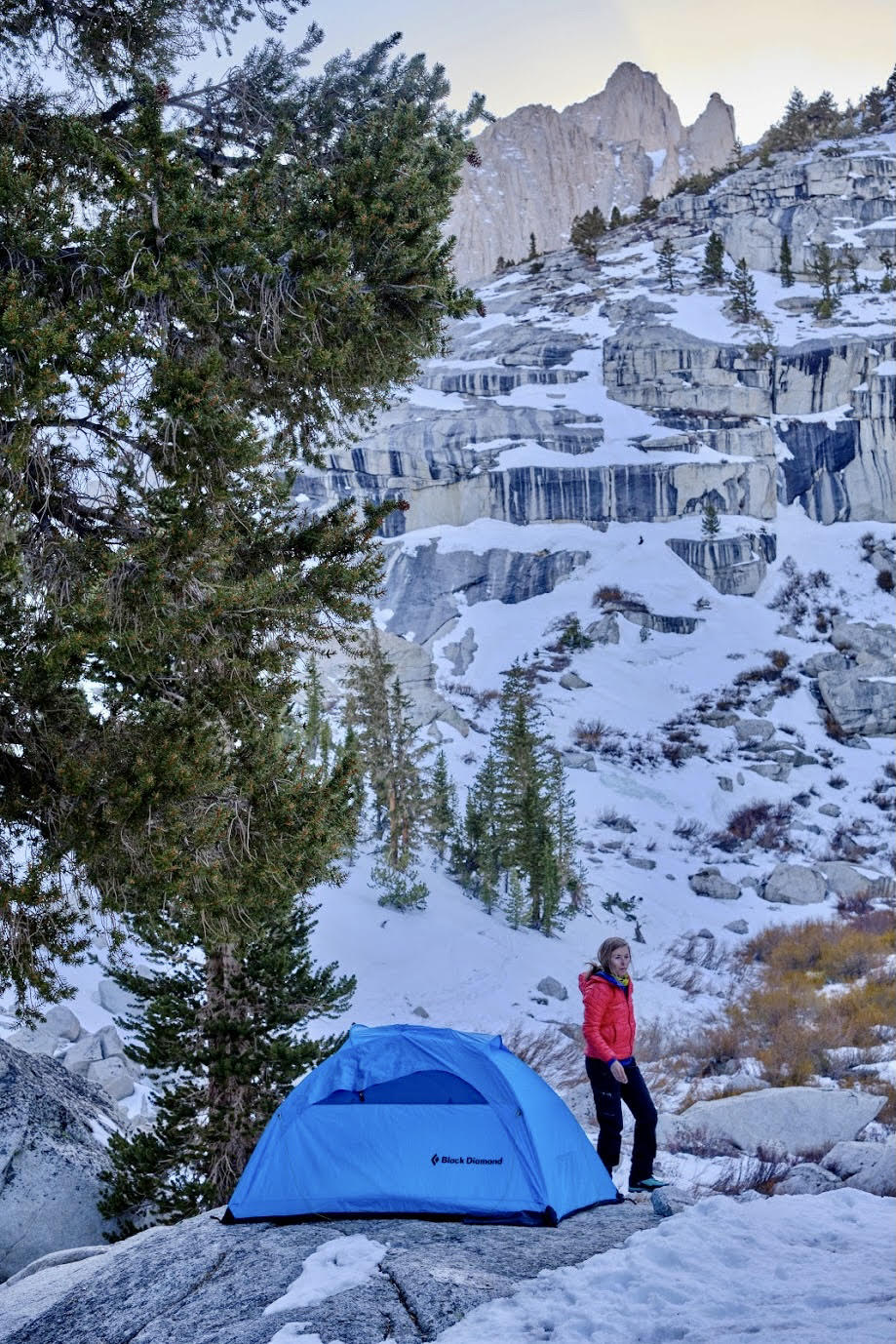 Woman camping outdoors in the winter. Snowcapped mountains visible in the background. 