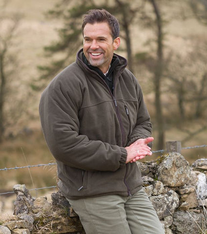 Man wearing Hoggs of Fife Ghillie II Waterproof Fleece Jacket smiling and sitting on a stone wall outdoors