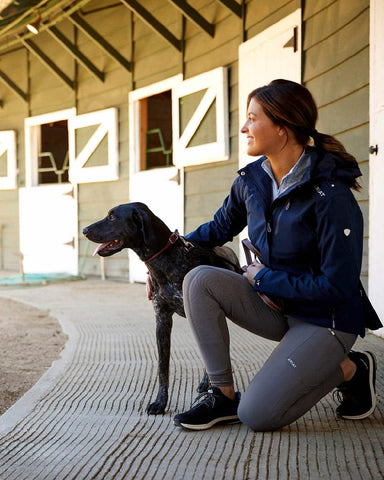 Woman wearing Ariat jacket outdoors bending down to tend to dog
