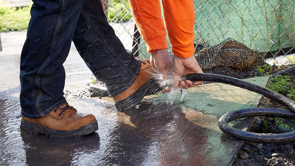 A hose being used to clean work boots outside