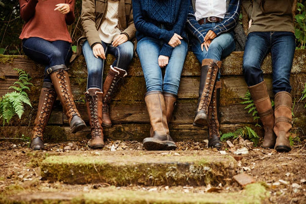 5 people sitting in a row out in the countryside each wearing Ariat boots