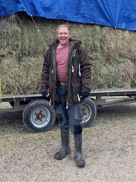 Farmer Ruben wearing his new Deerhunter Muflon jacket, smiling in front of a pile of hay.