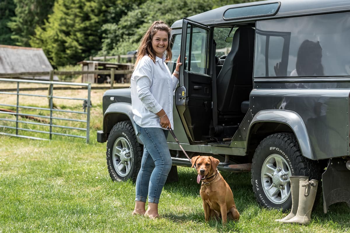 A woman with a brown dog posing next to a dark green 4x4 vehicle.
