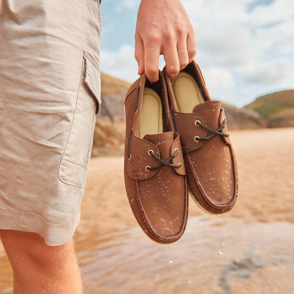 Dubarry Portarthur Oyster Windseeker Deck Shoes in cafe colour being held up against a warm sandy background