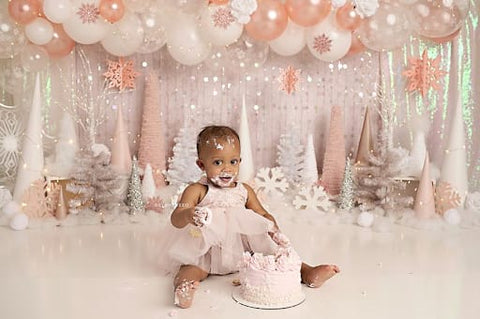 Baby girl sitting in front of a birthday backdrop with a pink smash cake in front of her