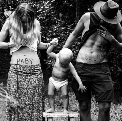 Woman with "baby" painted on her belly, toddler with "banana" painted on his belly, man with "beer" painted on his belly