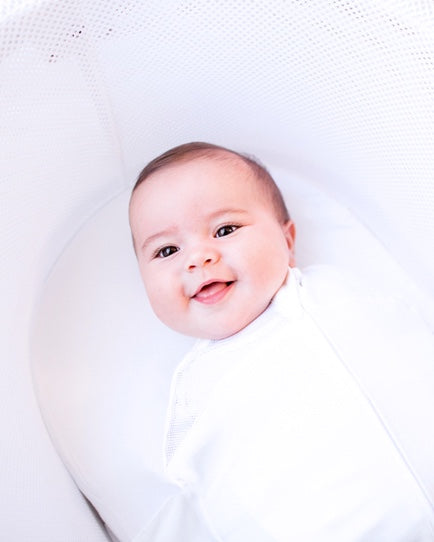 A baby smiles while swaddled in a SNOO Smart Sleeper.