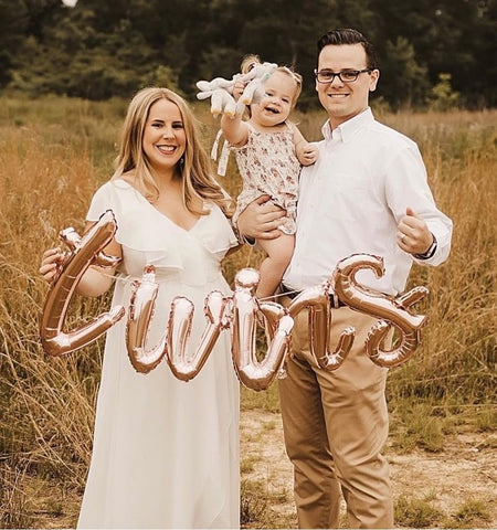 A family of three poses with balloons that spell out "twins"