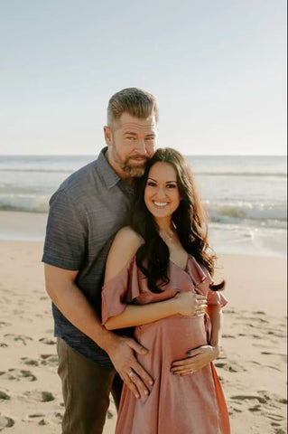 A pregnant woman shows off her bump and poses with her partner in a beach pregnancy announcement