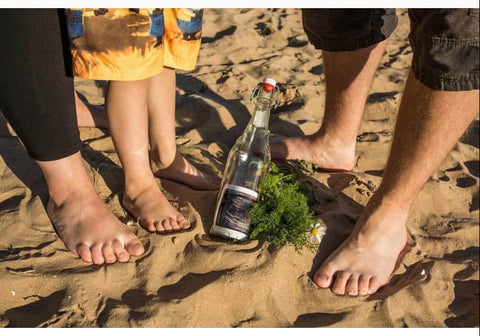 A beach pregnancy announcement that features a bottle with an ultrasound photo inside of it on the sand
