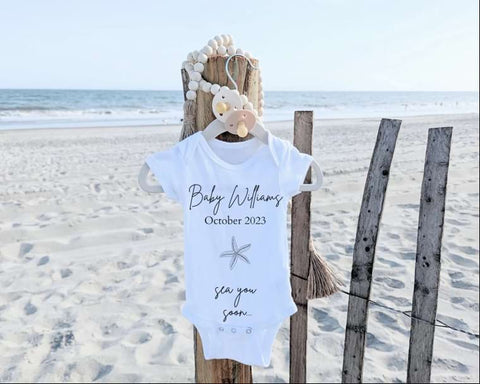 A baby onesie hangs on the beach to announce a pregnancy