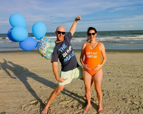 A couple poses with balloons in a beach pregnancy announcement