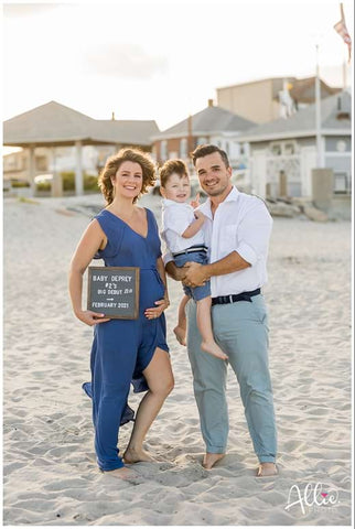 A family poses with a letterboard to announce a pregnancy on the beach