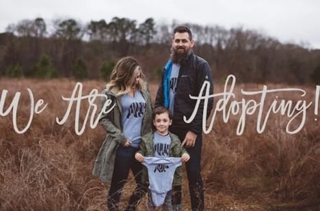 Family wearing matching bear shirts holds a matching onesie to announce adoption