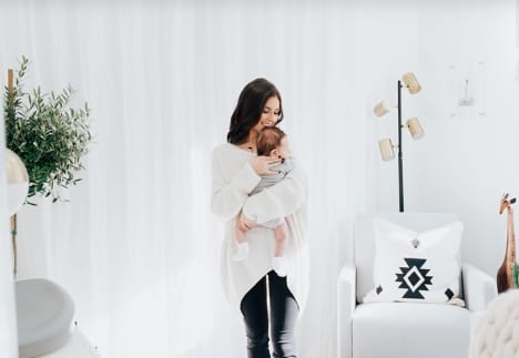 Mom and baby stand in an all-white nursery