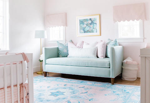 A pale pink baby nursery with a light blue couch and light blue-patterned rug.