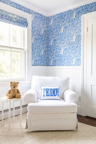 A blue baby nursery with a blue leaf-print wallpaper and matching leaf-print window shades.