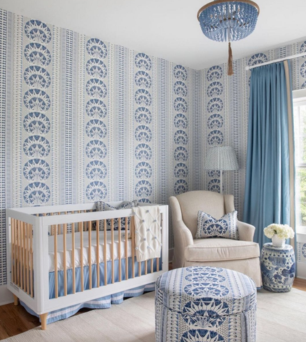 A baby nursery with a bold blue-and-white print wallpaper—the same pattern appears on a pillow and ottoman in the room.