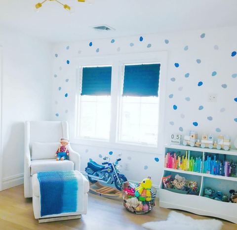 A baby nursery with blue polka-dot wallpaper and ombre blue window shades.