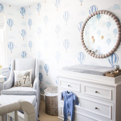The corner of a nursery with white-and-blue hot-air-balloon-printed wallpaper.
