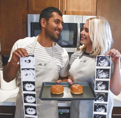 A couple poses holding ultrasound photos and a tray with two buns on it
