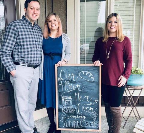 Family posing by a chalkboard announcing a surrogacy pregnancy