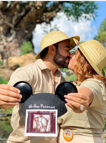 A couple dressed in safari gear holds Mickey ears and a sonogram in a Disney pregnancy announcement