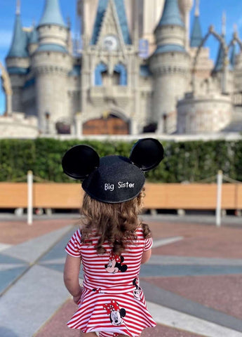 A Disney pregnancy announcement photo where a little girl wears Mickey ears that say "Big Sis" at the Magic Kingdom 