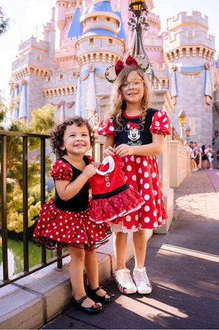 Disney pregnancy announcement photo: Two big-sisters-to-be are dressed like Minnie Mouse and hold a smaller Minnie dress at one of the Disney parks