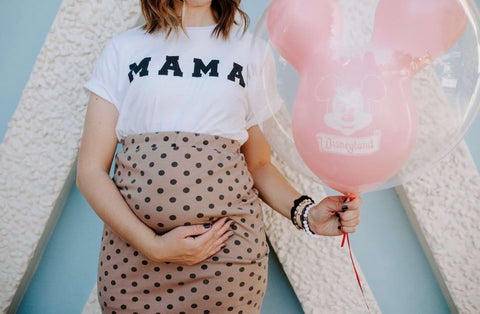 Disney pregnancy announcement photo: Pregnant woman wears a shirt that says mama and holds a pink Mickey Mouse balloon